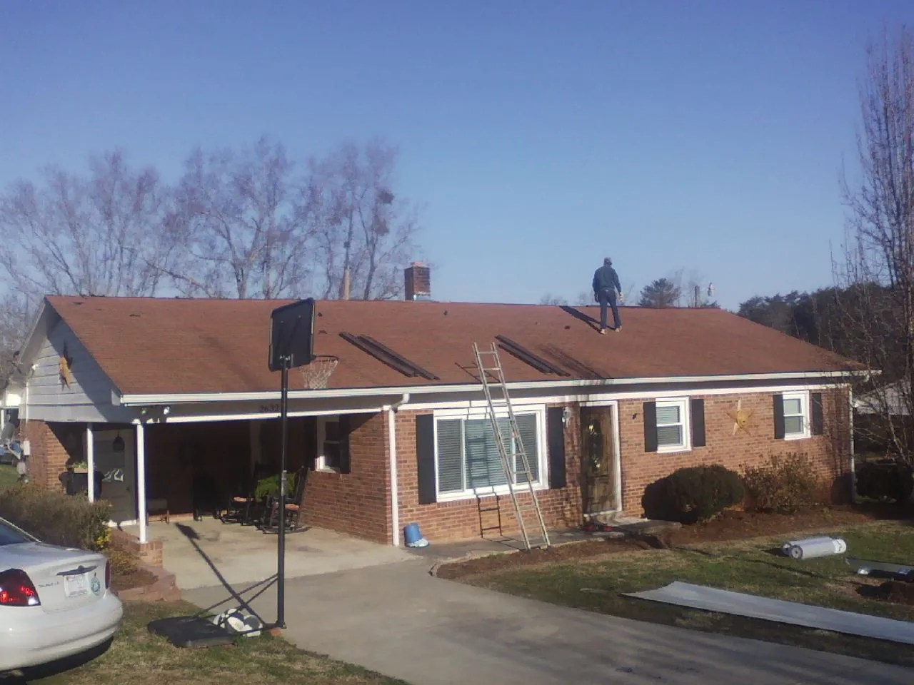 Roofer stripping a shingle roof on a brick ranch before metal panels in Livingston