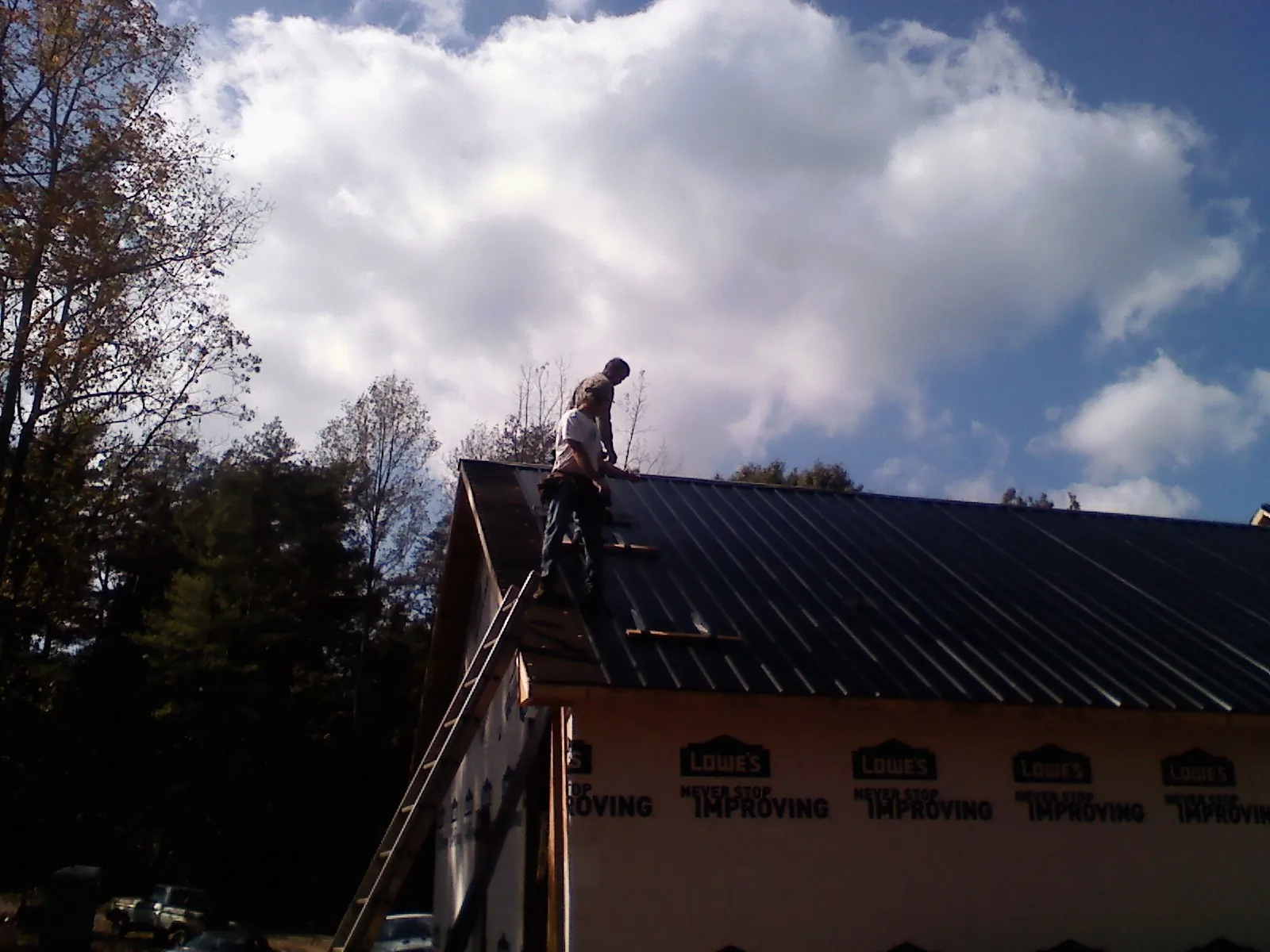 Roofer fastening dark metal panels high against a cloudy sky, from a Roof Inspection job in Livingston